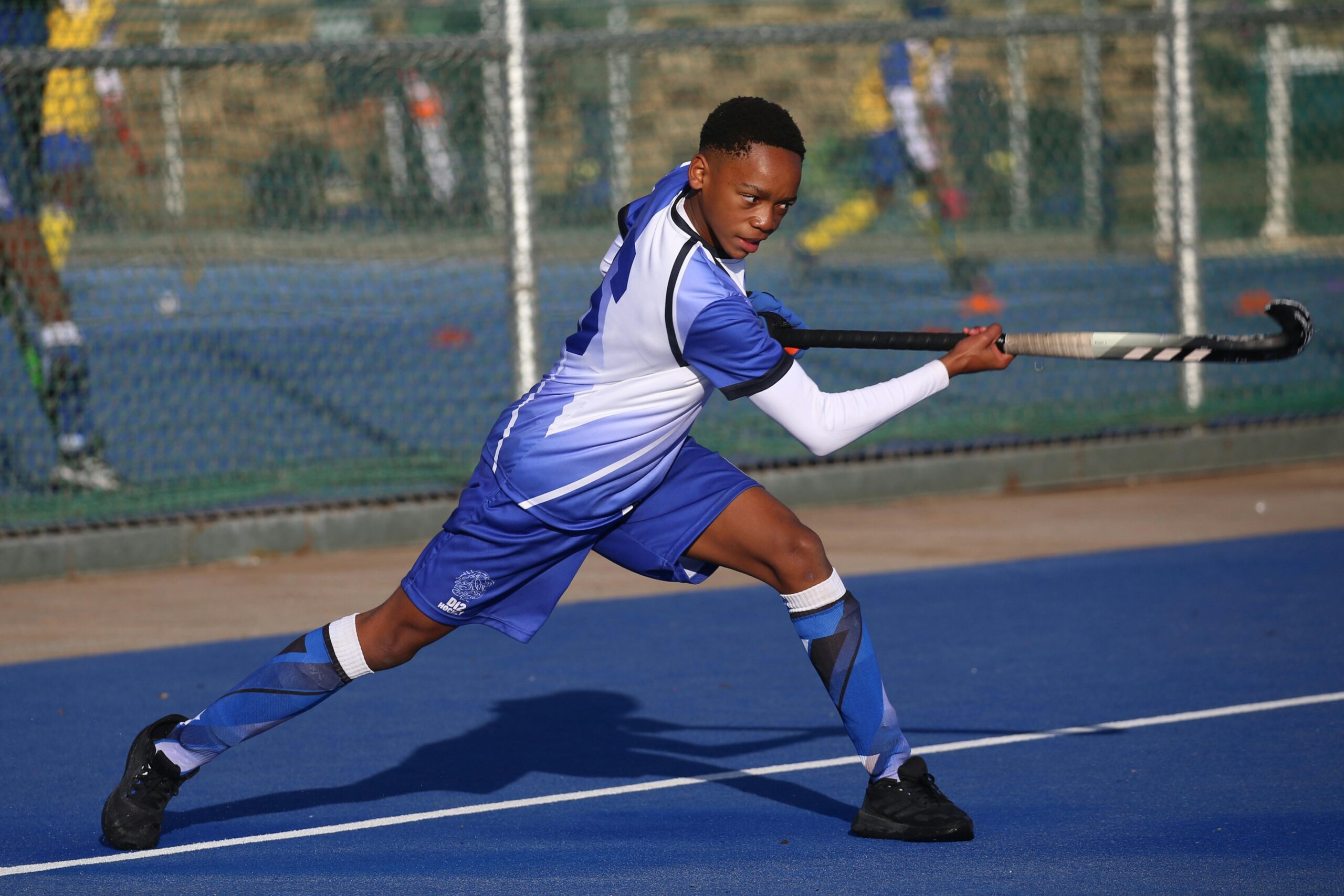 Junger m&Atilde;&curren;nnlicher Athlet, der auf einem leuchtend blauen Feld einen kraftvollen Feldhockeyschlag ausf&Atilde;&frac14;hrt.