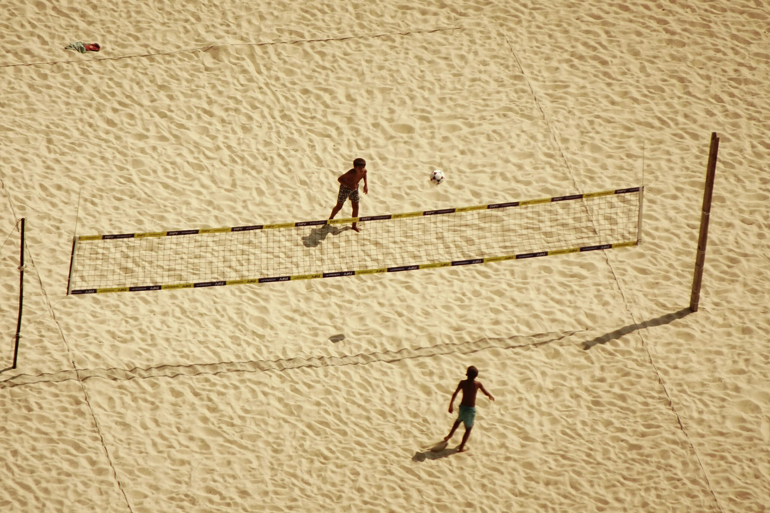 Zwei Personen spielen Volleyball an einem Sandstrand, von oben gesehen.